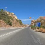 A scenic road in Crete, Greece, showing speed limit signs of 60 km/h and 30 km/h, along with a directional road sign. The image highlights the local traffic regulations and road signage in a mountainous area under a clear blue sky.